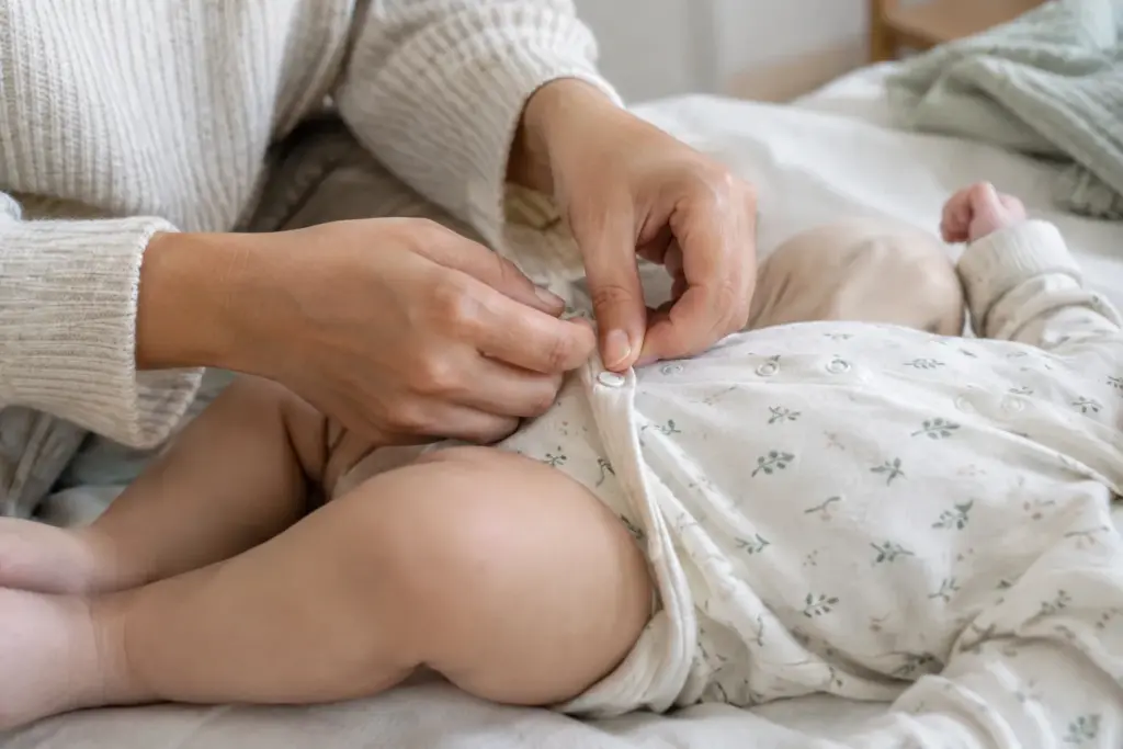 Un adulte ajuste délicatement une couche de vêtements en coton sur un bébé.