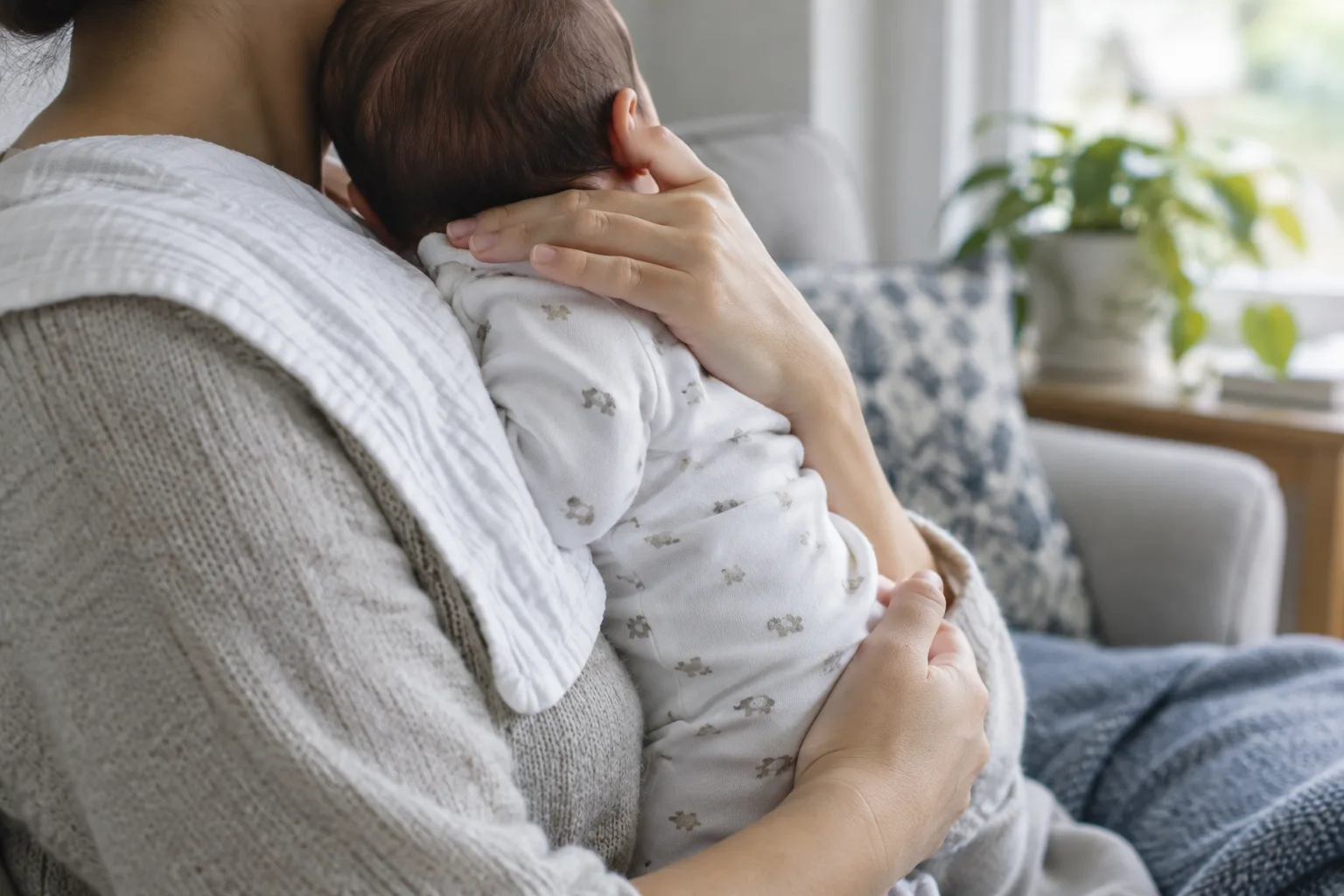 Un bébé est maintenu contre l’épaule d’un adulte qui soutient doucement son dos et sa nuque.
