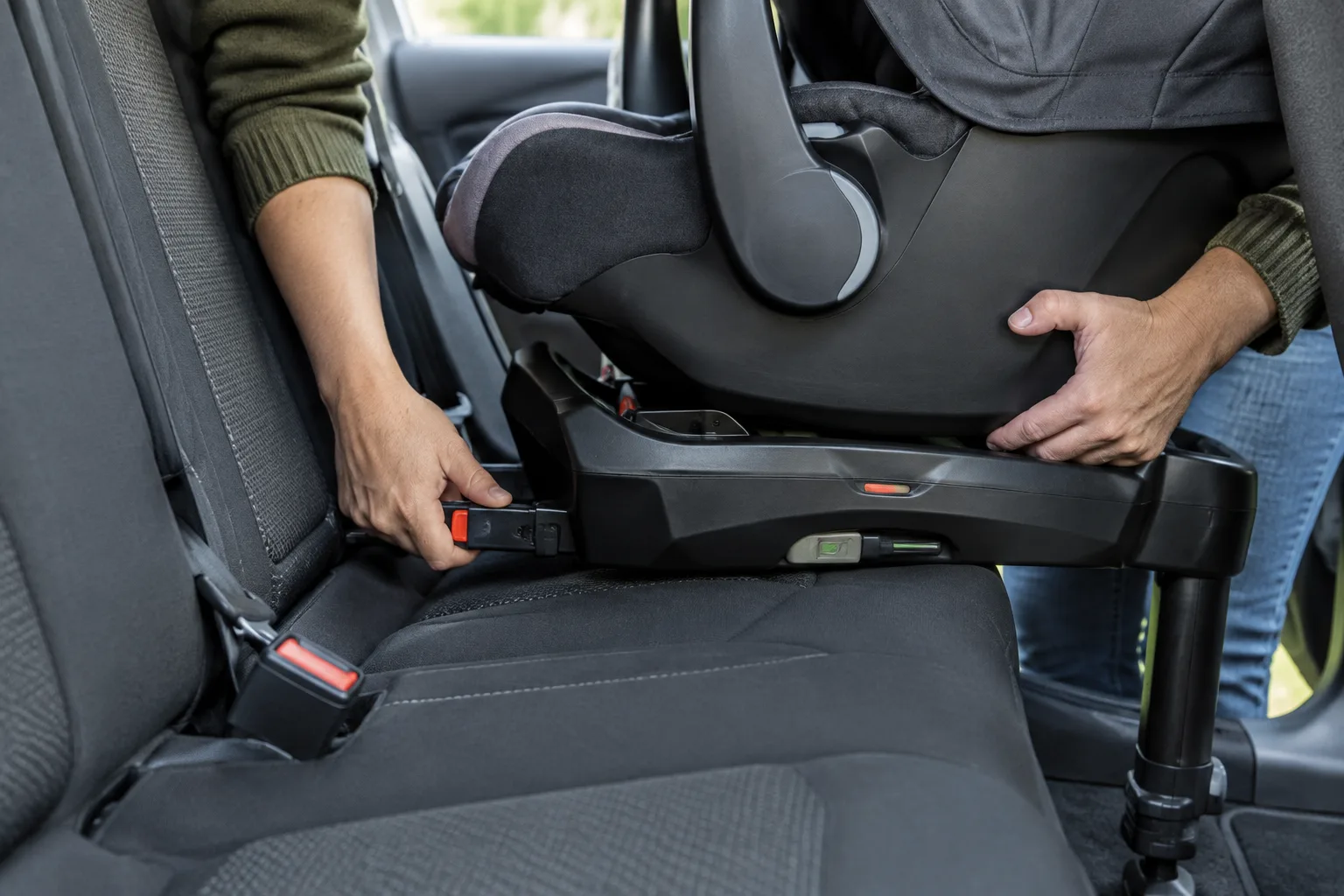 Des mains fixent un siège-auto pour bébé en suivant les points d’ancrage prévus.