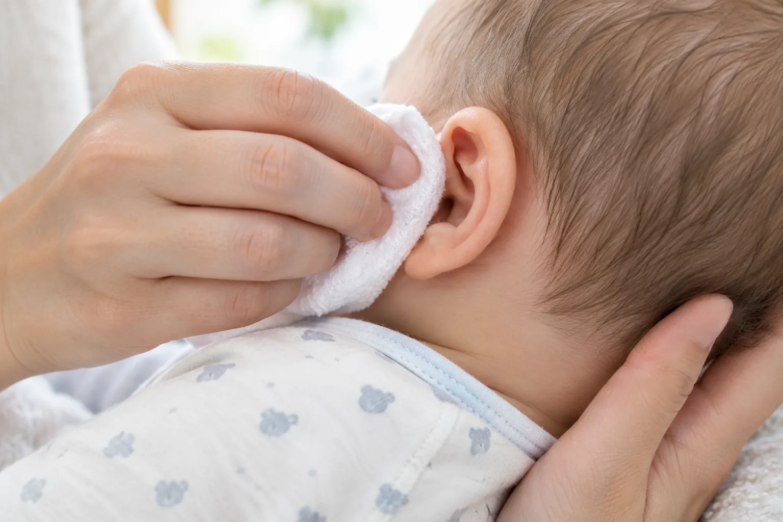 Un linge doux passe sur le pavillon de l’oreille d’un bébé, sans entrer dans le conduit auditif.
