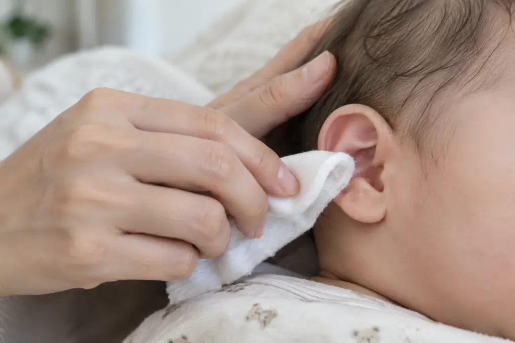 Une main nettoie doucement le contour de l’oreille d’un bébé avec un linge humide.