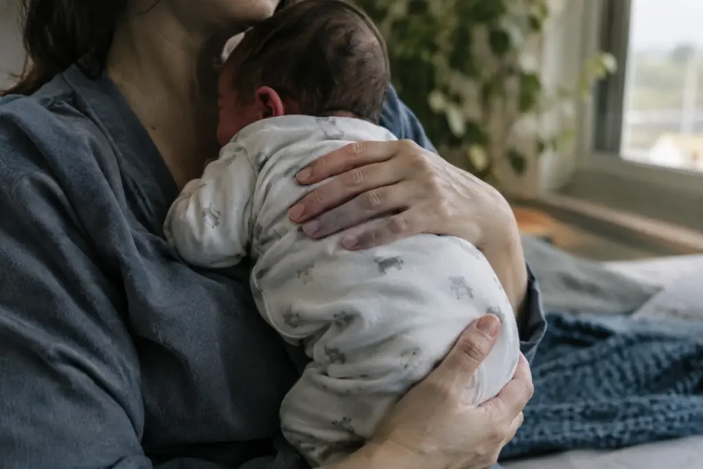 Un parent tient doucement son bébé contre lui dans une pièce calme.