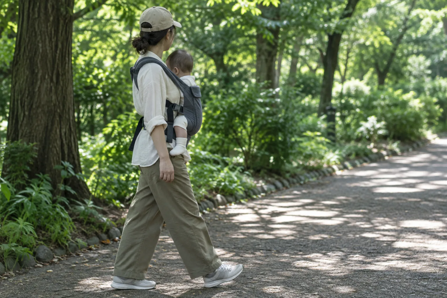 Un parent marche dans un parc ombragé avec son bébé installé dans un porte-bébé.