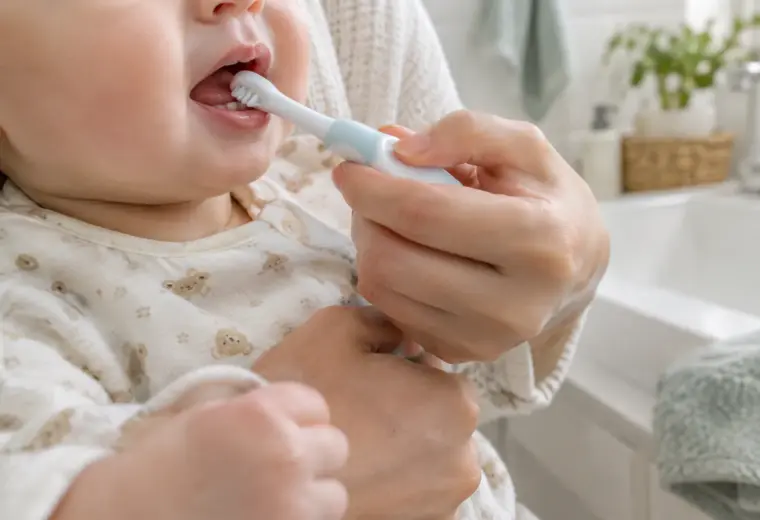 Un parent brosse doucement les premières dents de son bébé avec une petite brosse à dents.