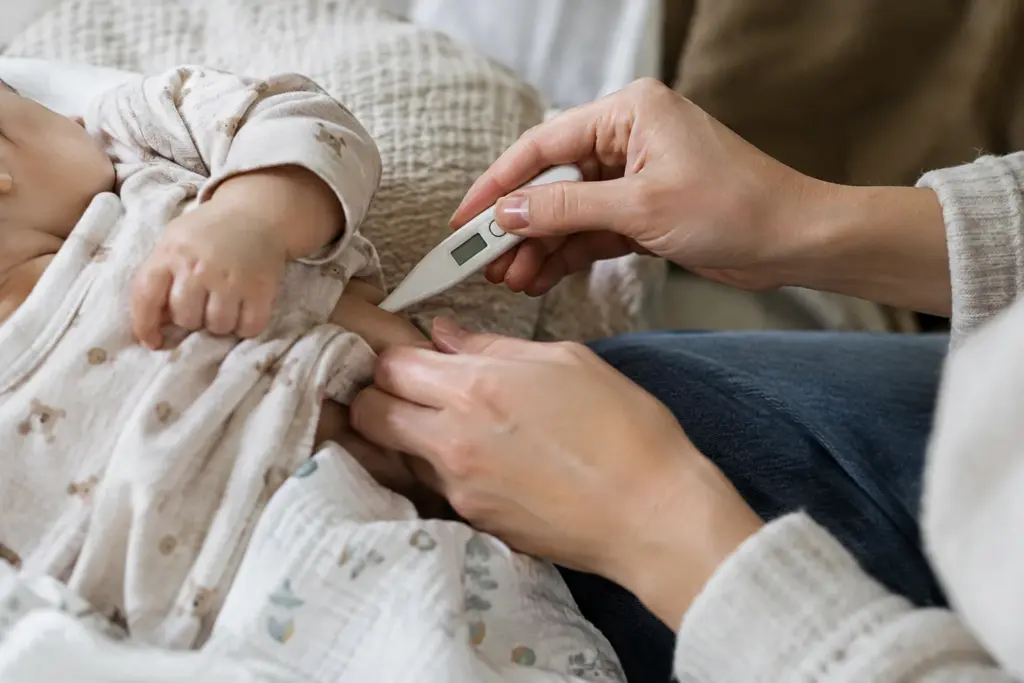 Un parent prend doucement la température d’un bébé avec un thermomètre électronique.