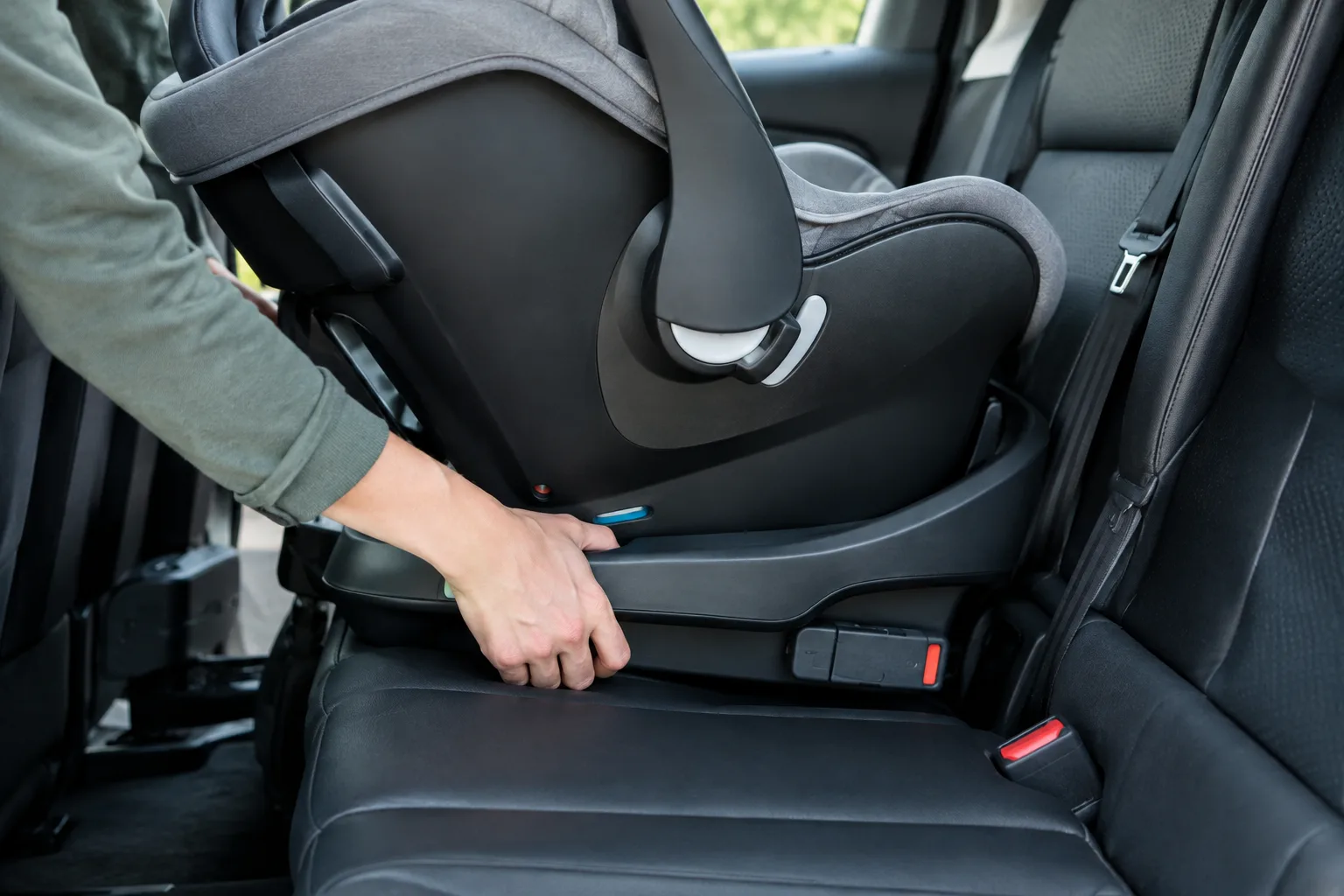 Des mains fixent un siège-auto dos à la route sur la banquette arrière.