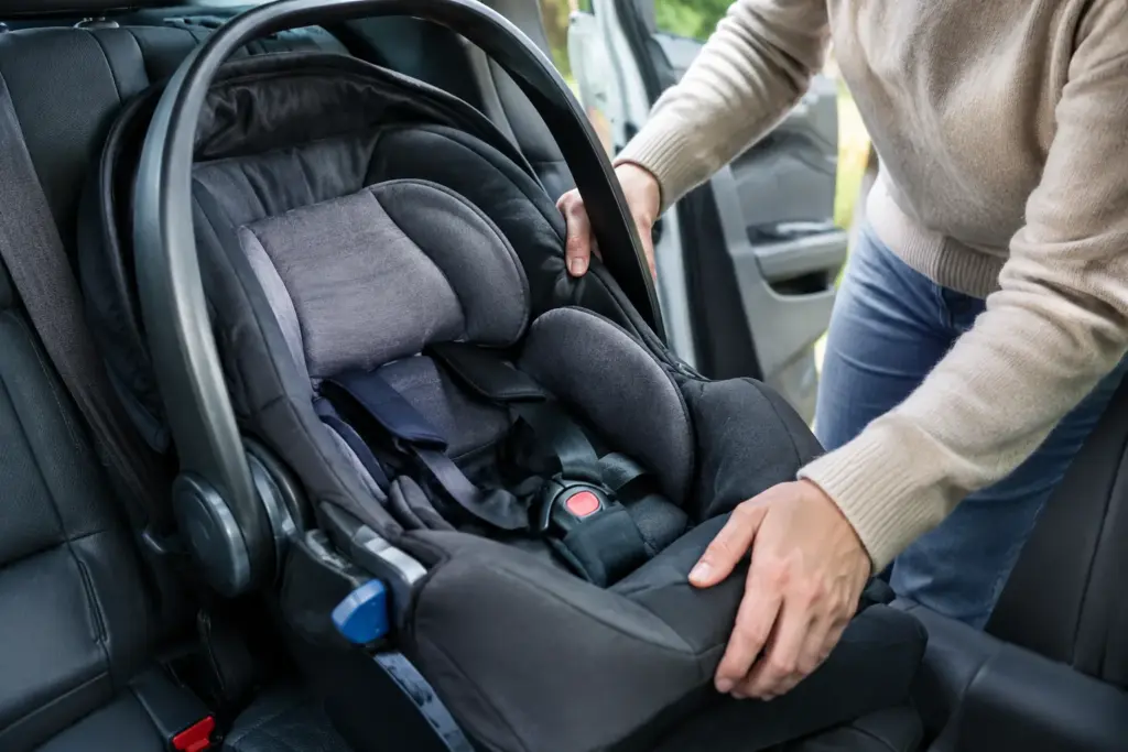 Un parent vérifie l’installation d’un siège-auto pour bébé sur la banquette arrière.