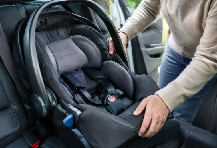 Un parent vérifie l’installation d’un siège-auto pour bébé sur la banquette arrière.